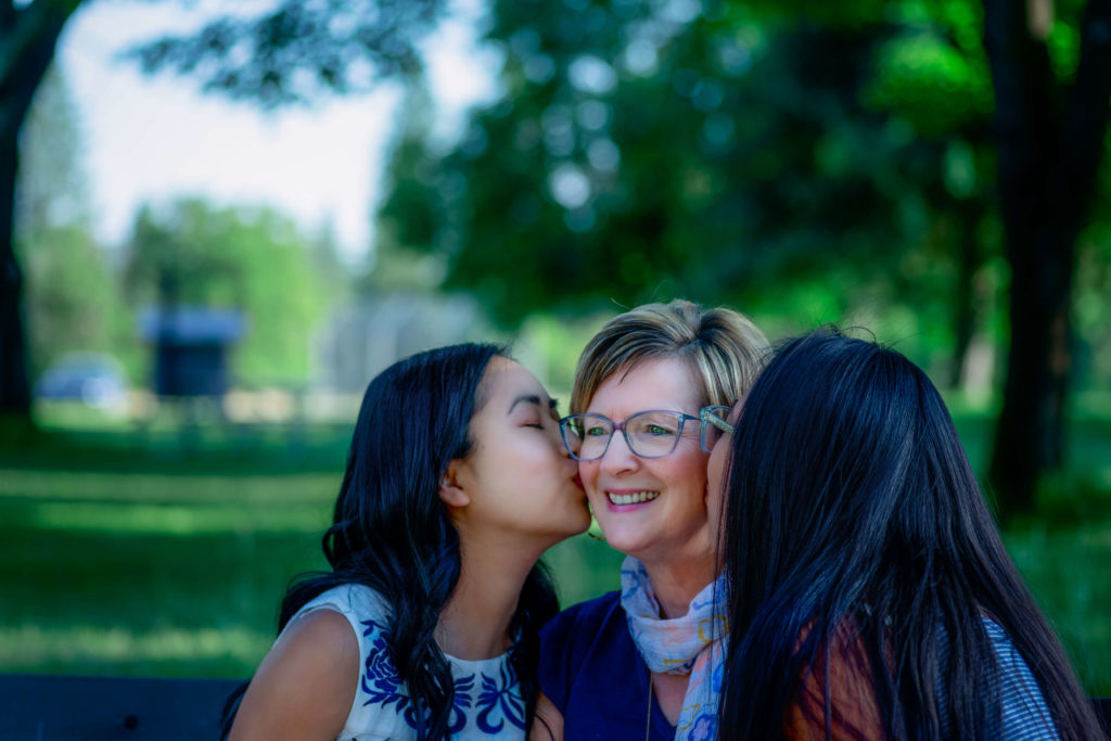 Daughters kiss mom on cheek during family photography session in Kettle Falls, Washington