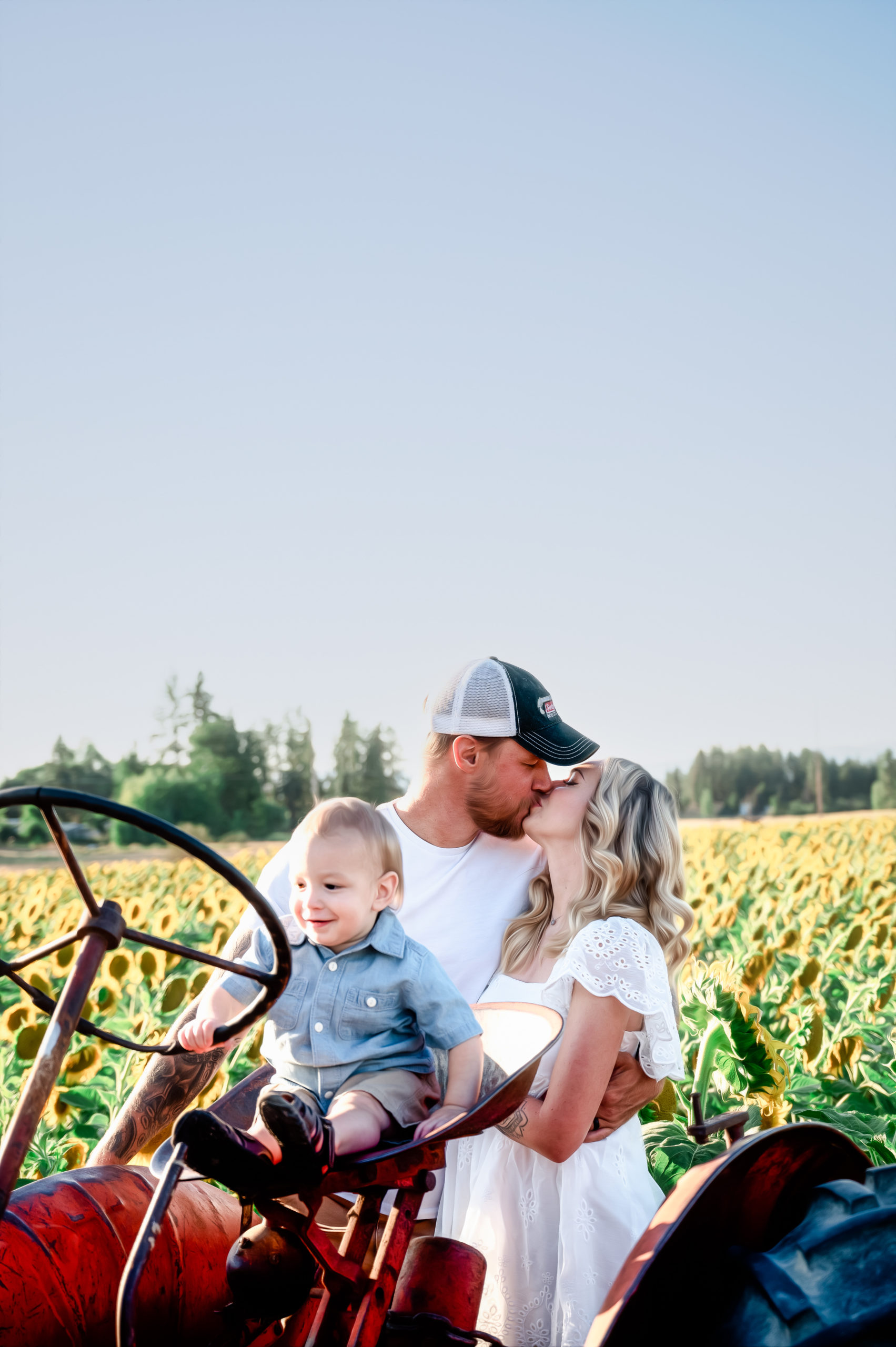 mom and dad sharing a kiss as their son sits on a tractors