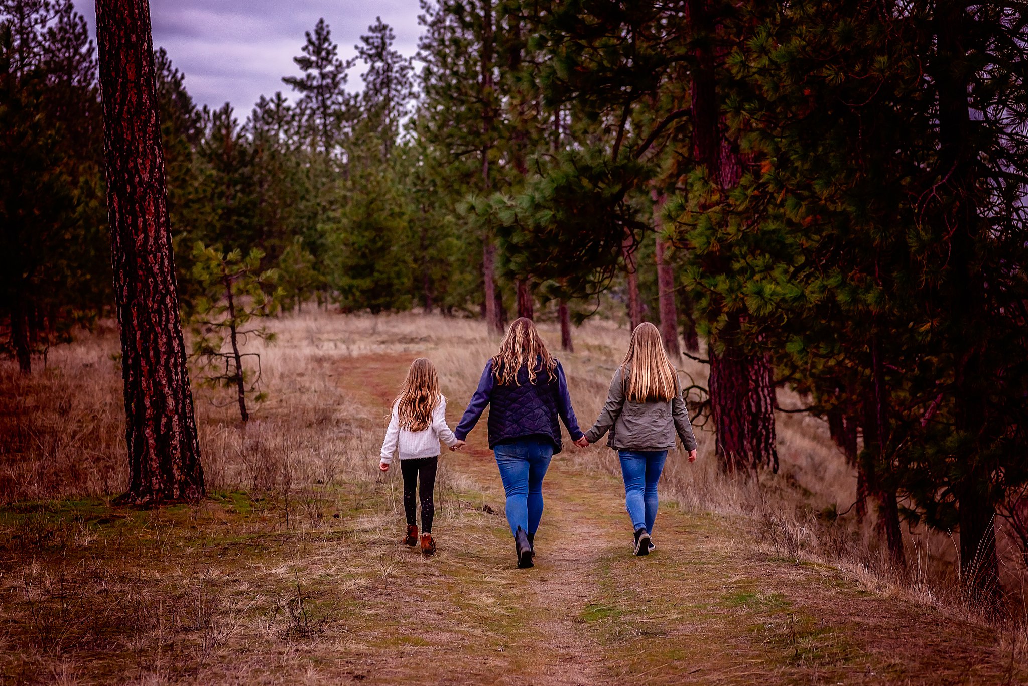 mom and daughters walking hand in hand through a field