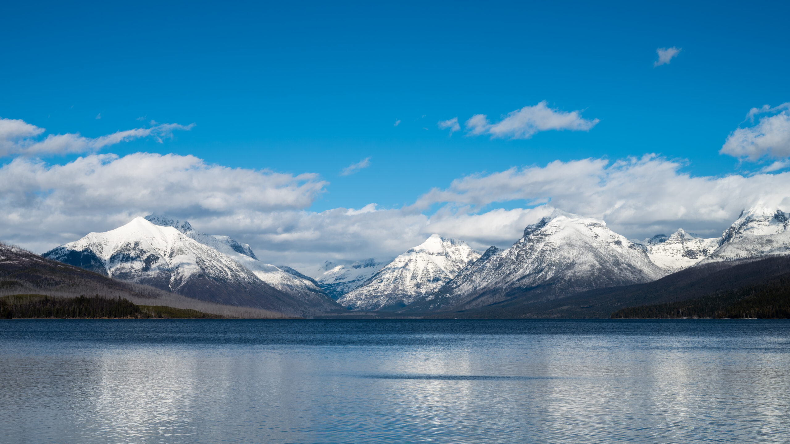 Lake McDonald in Glacier National Park reflecting snow‑covered mountains beneath a bright blue sky.